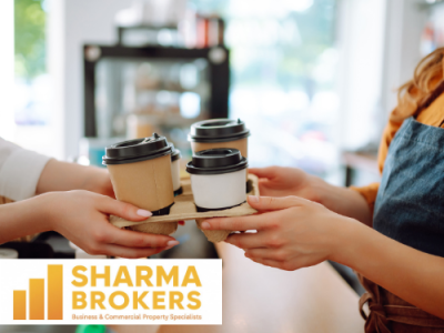A barista in a blue apron hands a tray of four takeaway coffees to a customer, with the SHARMA BROKERS logo